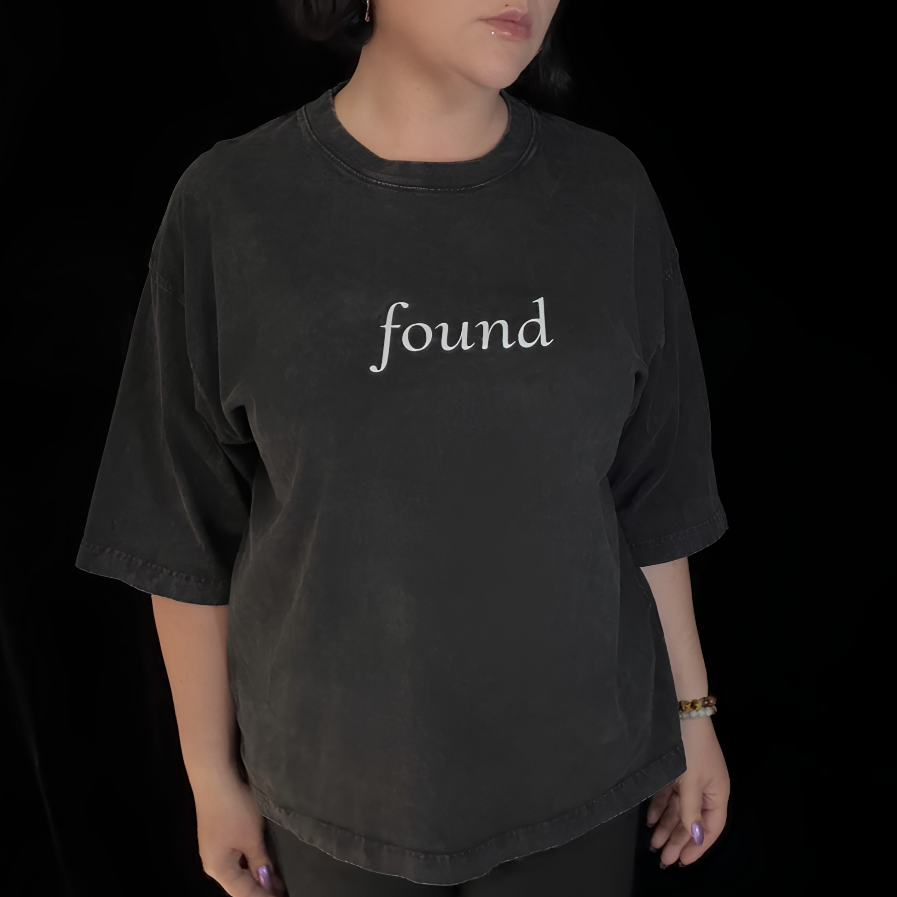 alt millennial woman wearing faded black boxy tee with text found on the center chest
