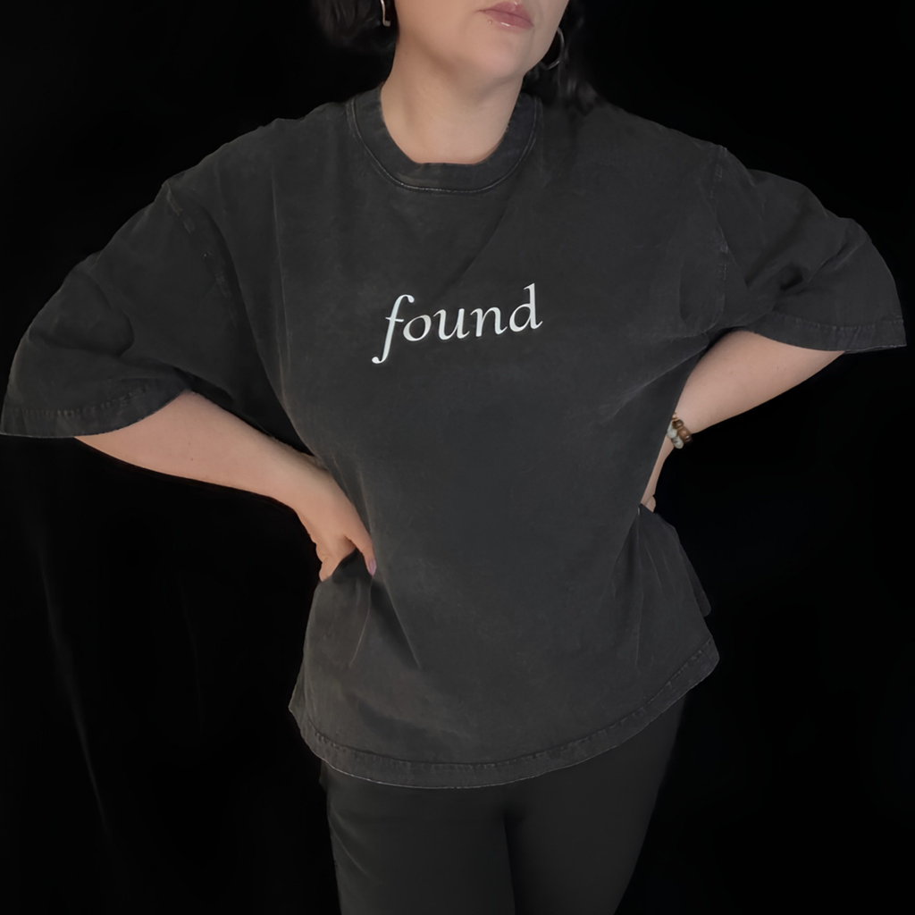 alt millennial woman wearing faded black boxy tee with text found on the center chest