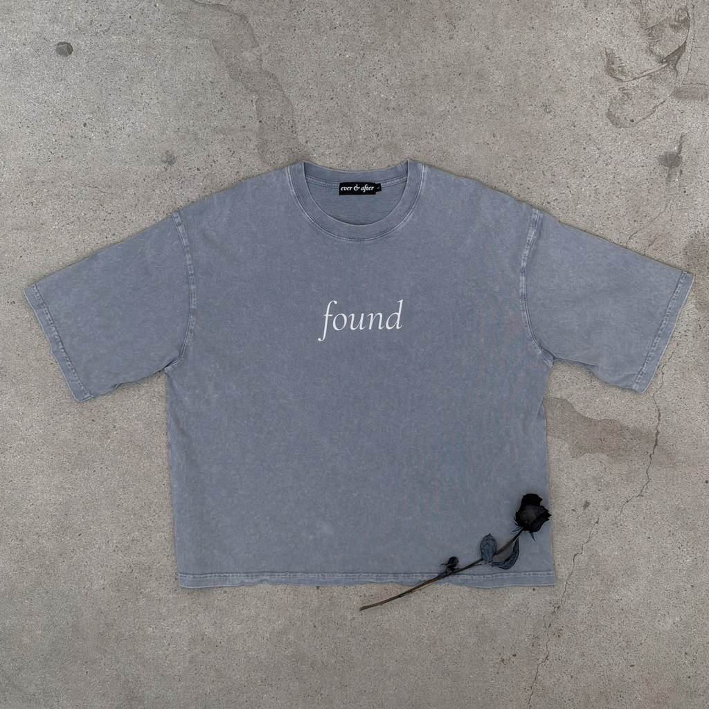 light gray boxy tee layflat on concrete with rose text found on center chest