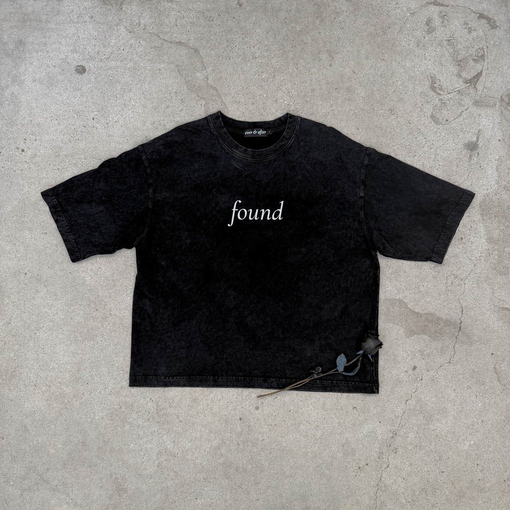 faded black boxy tee layflat on concrete with rose text found on center chest