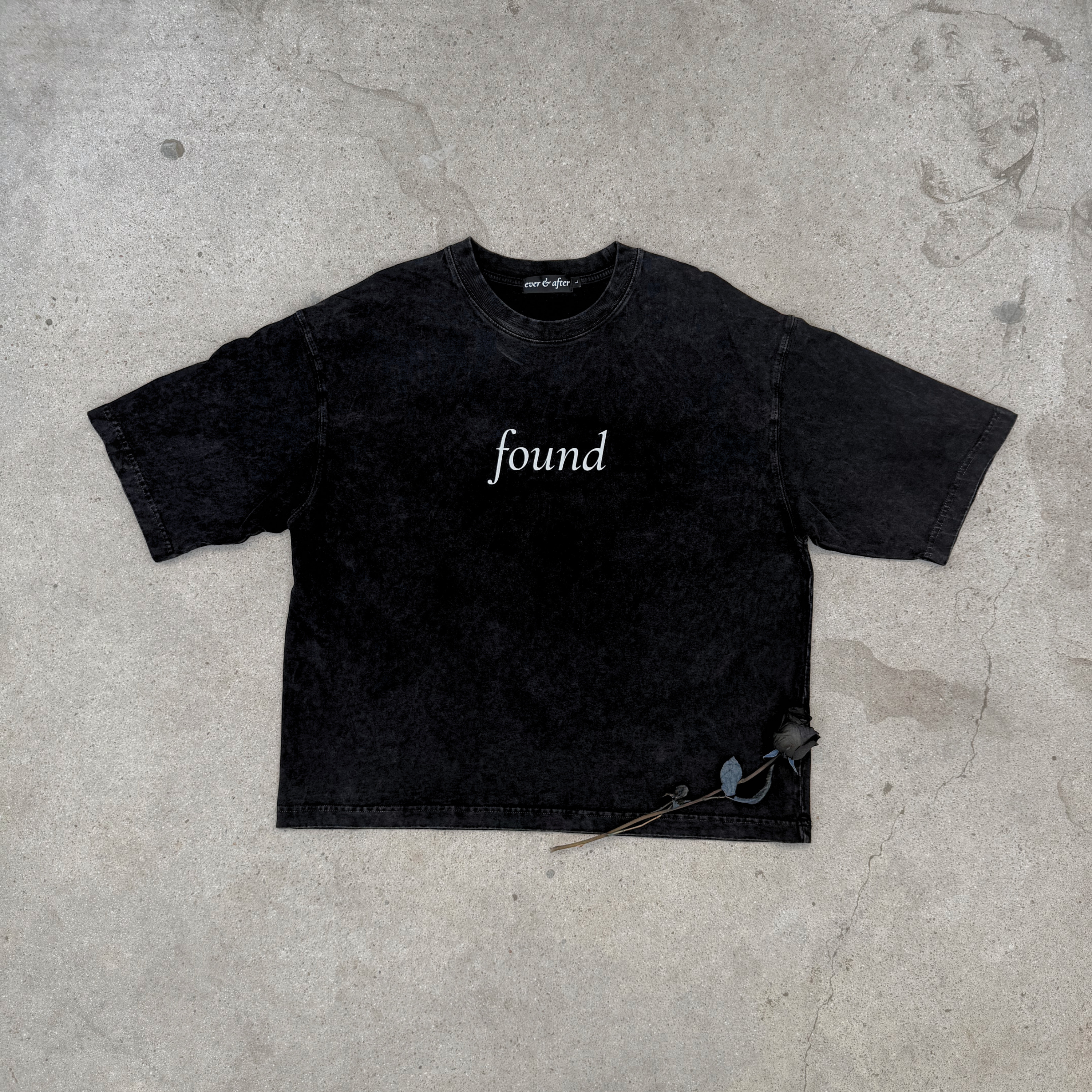 faded black boxy tee layflat on concrete with rose text found on center chest