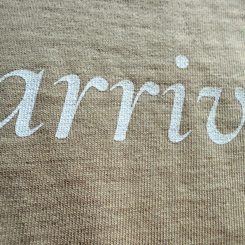 Text 'arrive' embroidered on a beige tee
