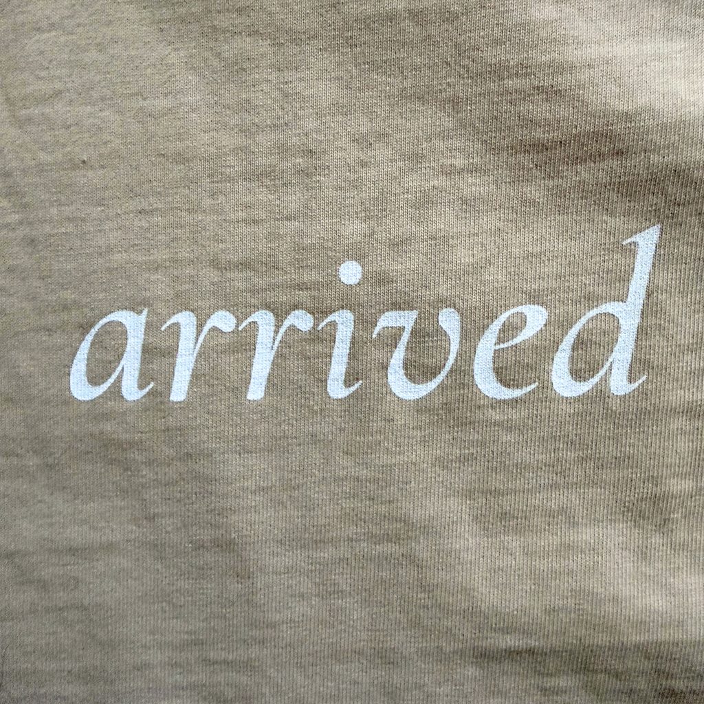 Text 'arrived' printed on a beige tee