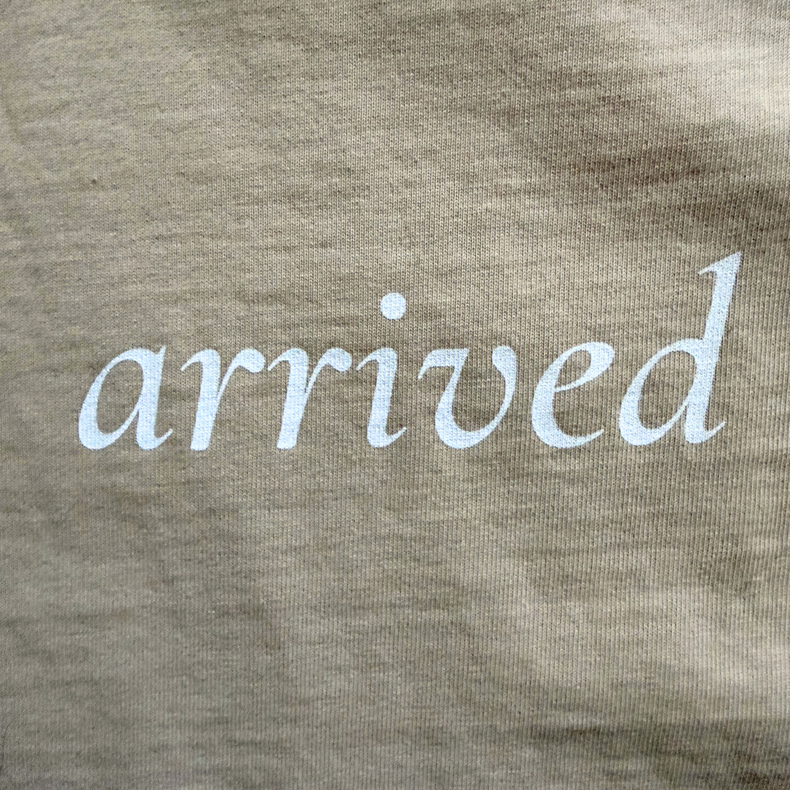 Text 'arrived' printed on a beige tee