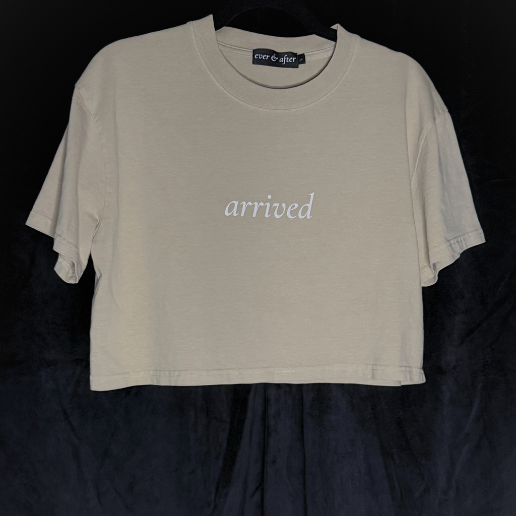 Beige t-shirt with 'arrived' text on a black background