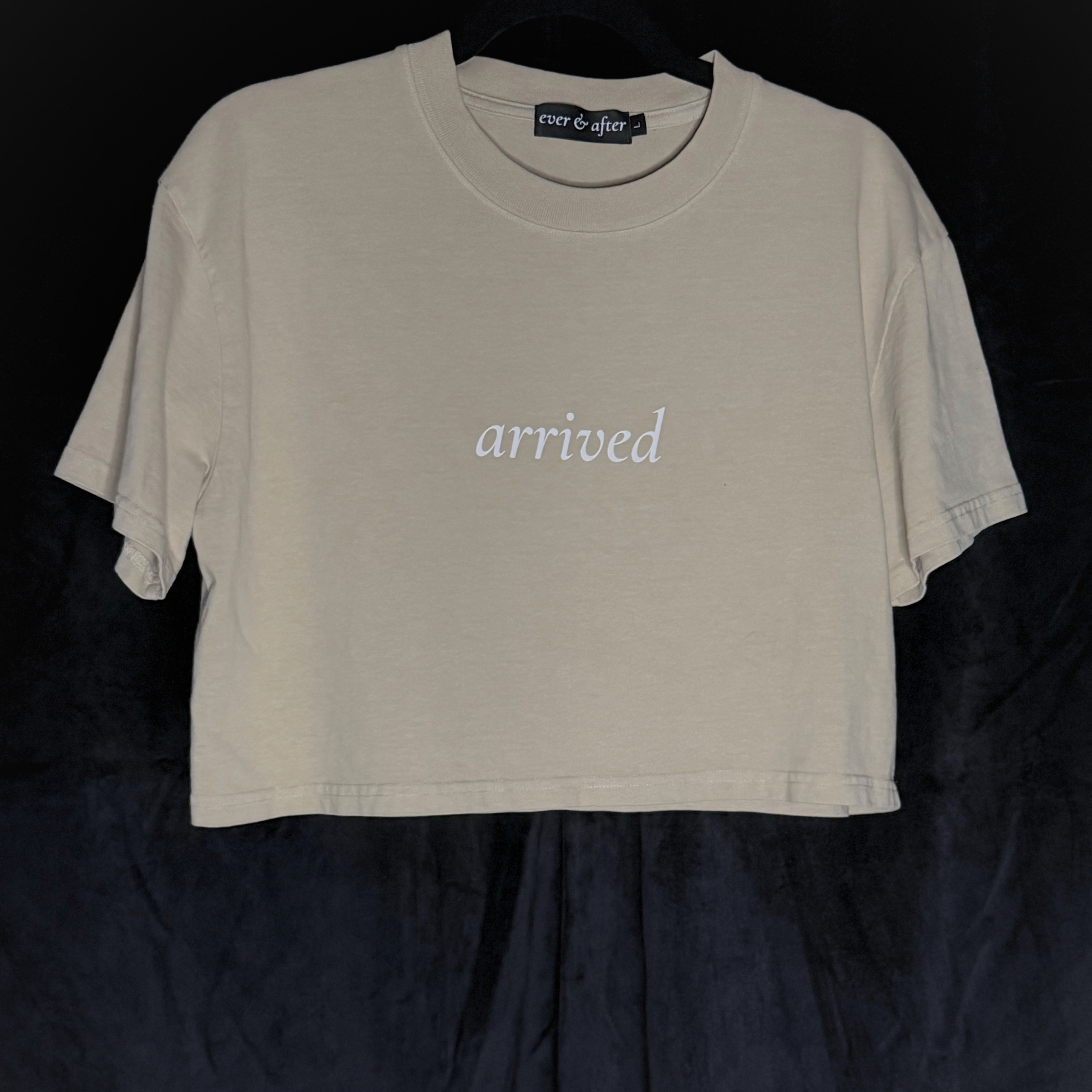 Beige t-shirt with 'arrived' text on a black background