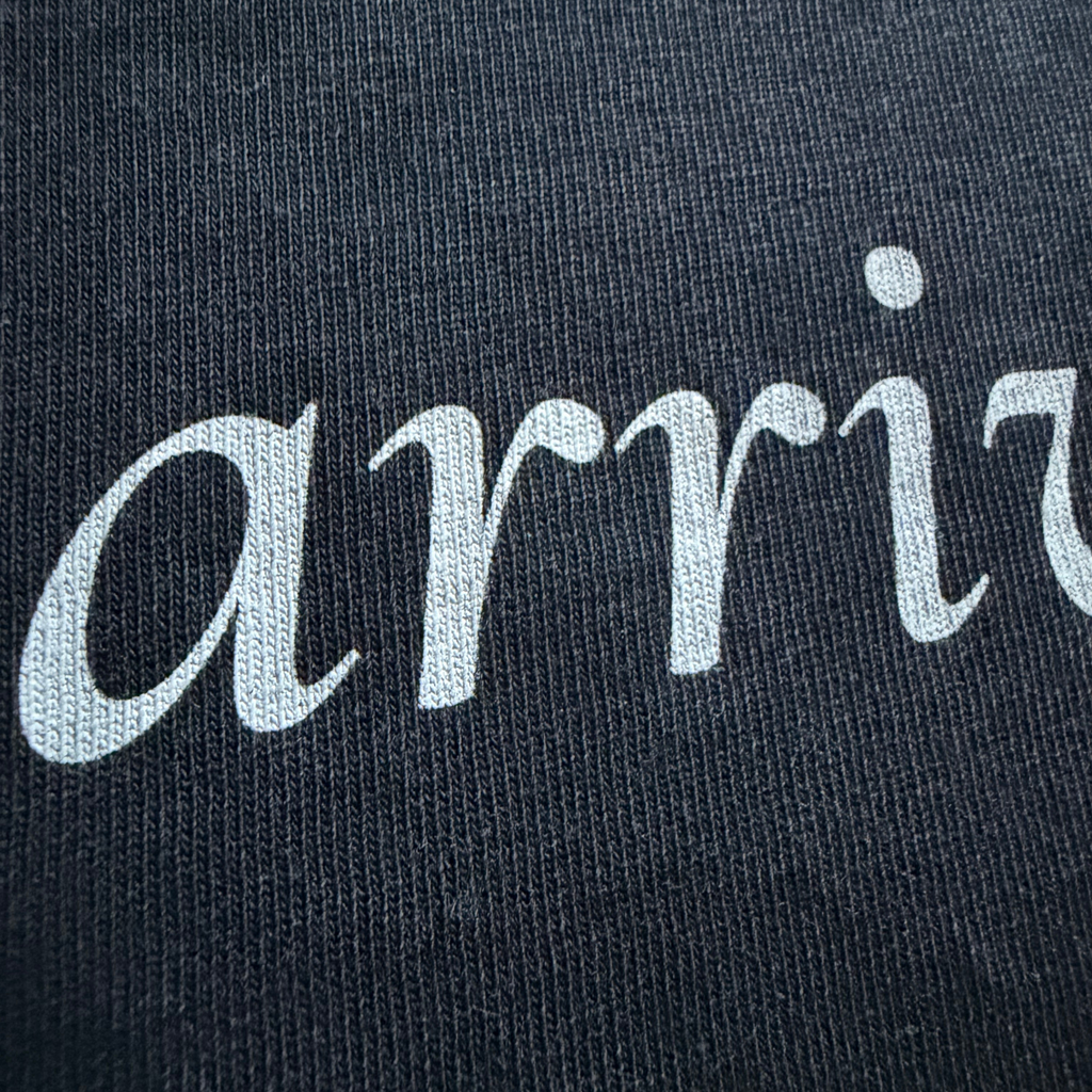 Text 'arrive' embroidered on a black fabric background