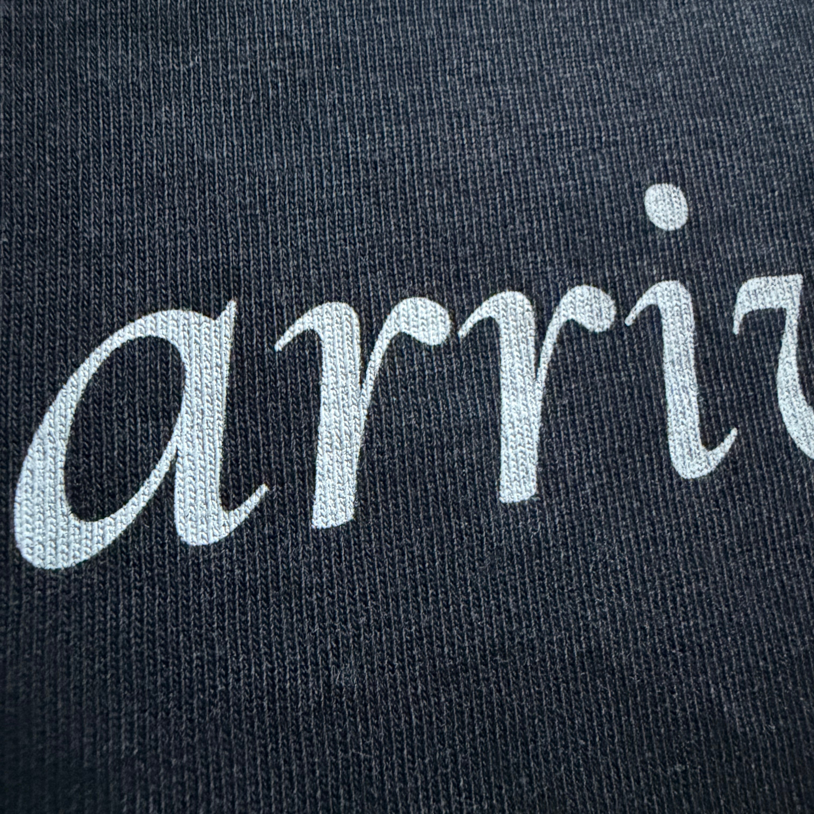 Text 'arrive' embroidered on a black fabric background