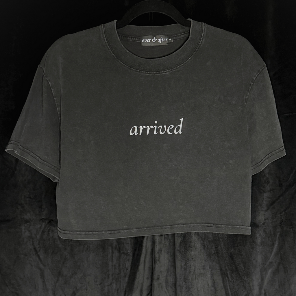 Black crop top with 'arrived' text on a dark background