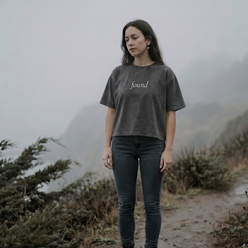 alt millennial woman standing on a foggy path wearing faded black boxy tee with text found on the center chest