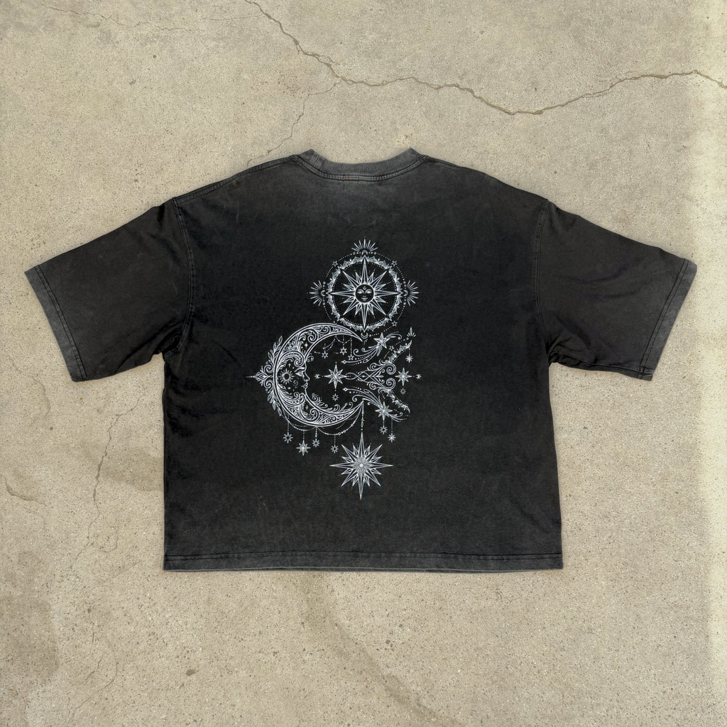 Black t-shirt with celestial design on a beige concrete surface