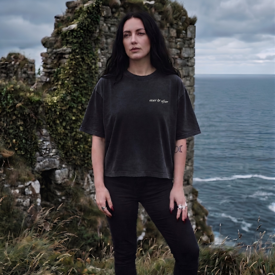 Person wearing a black t-shirt with text standing in front of ocean cliffs.