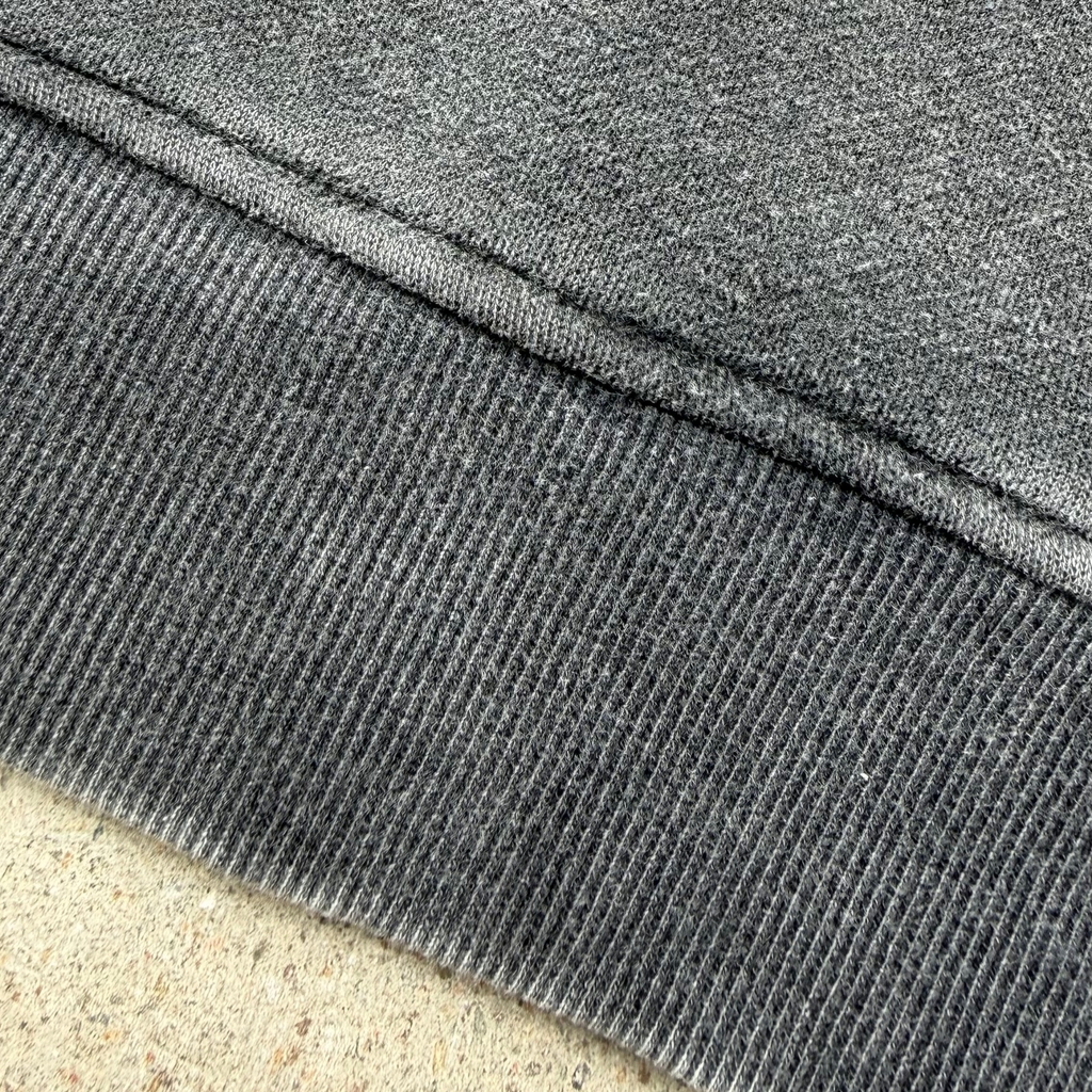 Close-up of a dark gray ribbed knit fabric cuff with a diagonal seam, showing the texture and weave detail.
