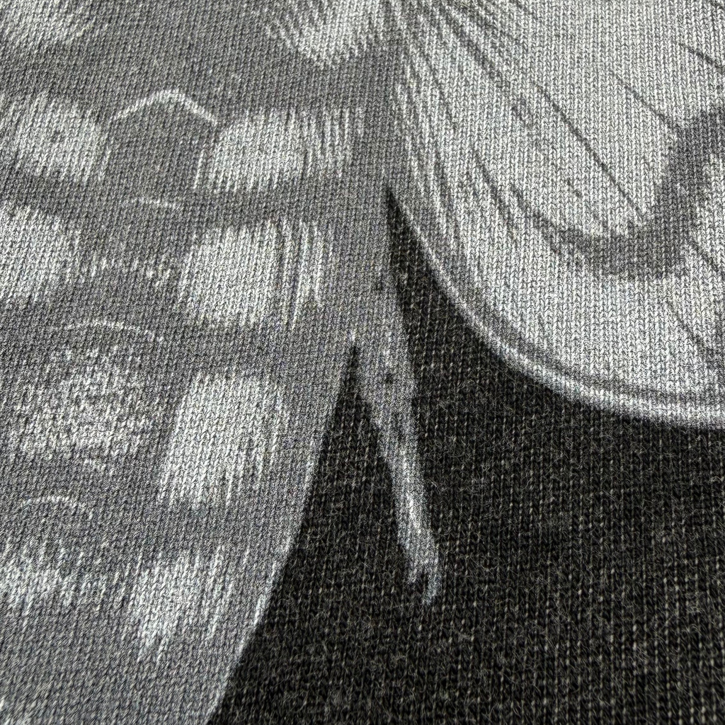 Close-up of a black and gray printed textile pattern showing part of a stylized insect or wing design on a woven fabric background.