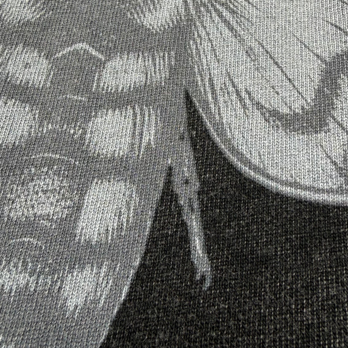 Close-up of a black and gray printed textile pattern showing part of a stylized insect or wing design on a woven fabric background.