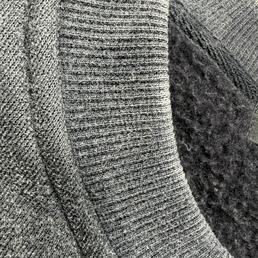 Close-up of a gray knit garment showing ribbed texture, a lighter heather gray ribbed band, and a dark charcoal fuzzy inner lining.