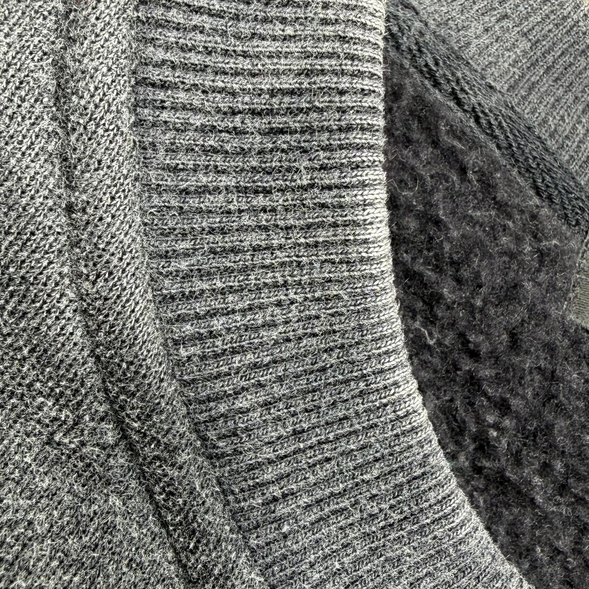 Close-up of a gray knit garment showing ribbed texture, a lighter heather gray ribbed band, and a dark charcoal fuzzy inner lining.
