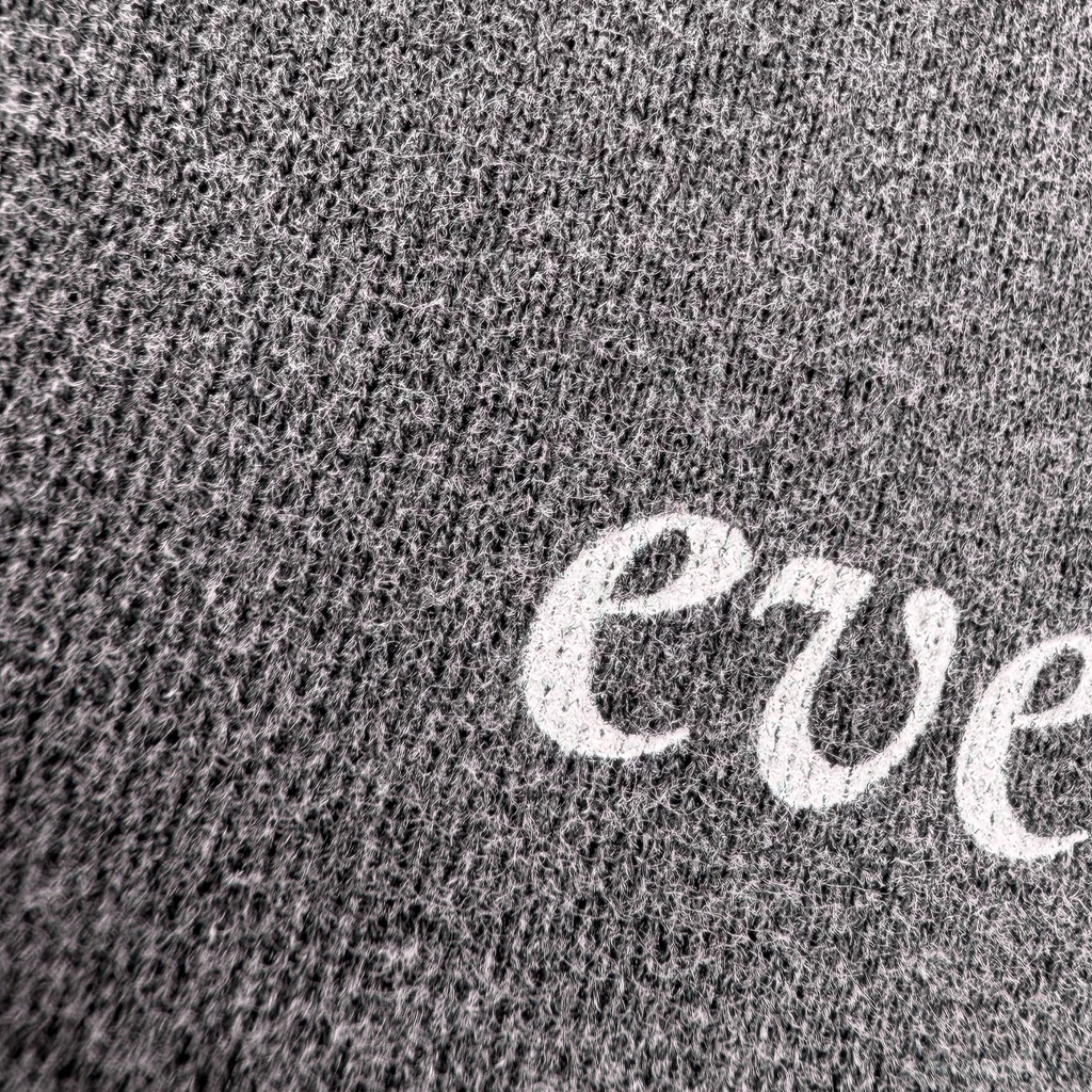 Close-up of a dark gray heather knit fabric with a white embroidered script letter 'e' partially visible.