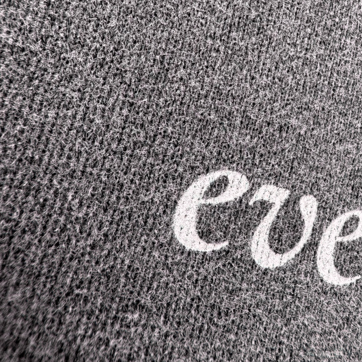 Close-up of a dark gray heather knit fabric with a white embroidered script letter 'e' partially visible.