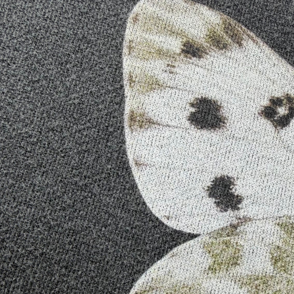 Close-up of a textured fabric featuring a white butterfly wing pattern with dark spots on a dark gray background.