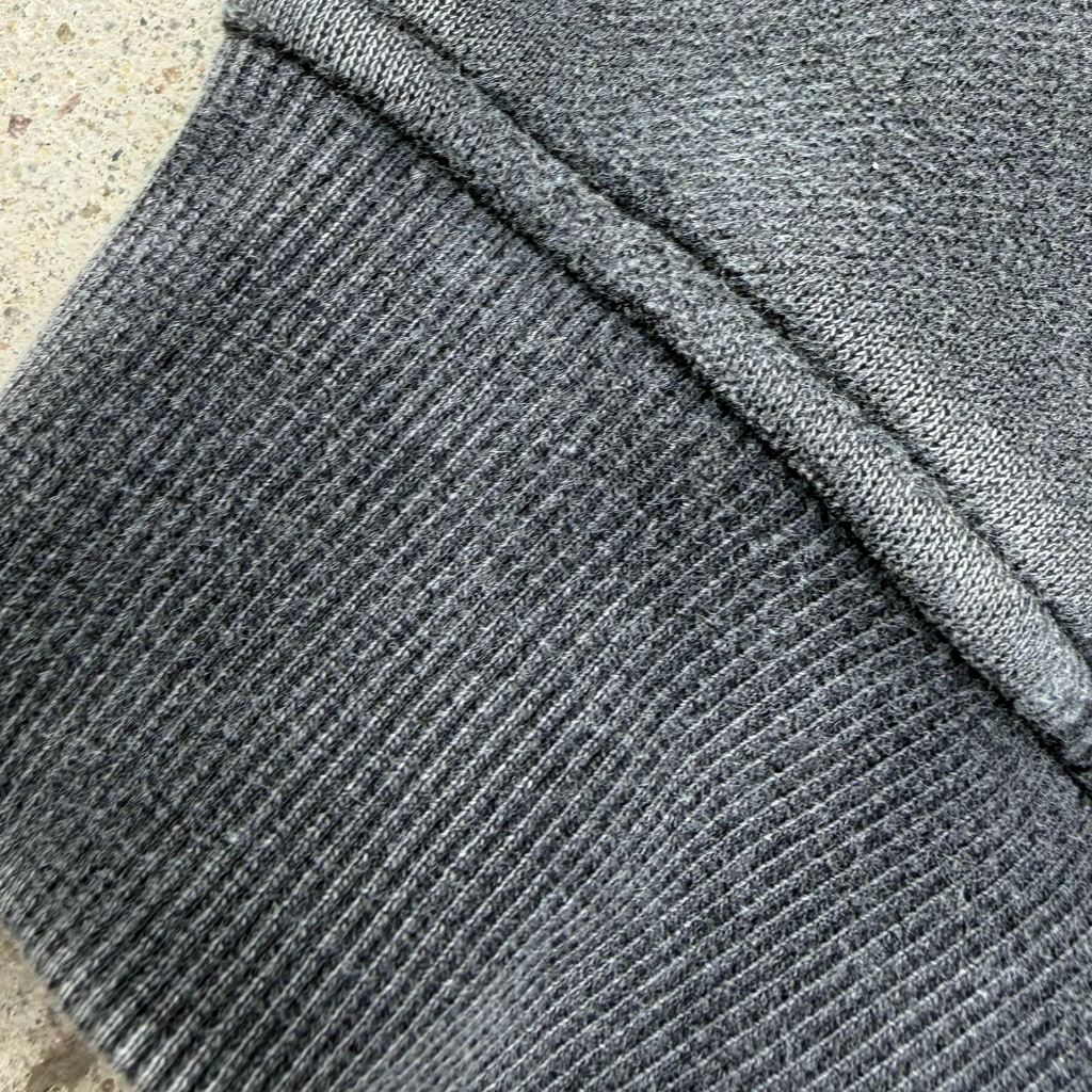 Close-up of a dark gray ribbed knit fabric, showing the detailed texture and stitching of a garment.