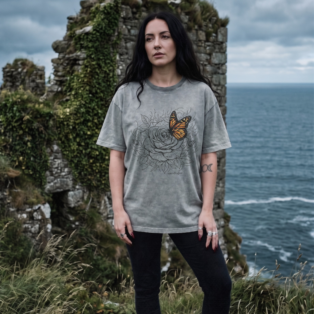 Woman wearing a gray t-shirt with a graphic design standing in front of ocean cliffs.
