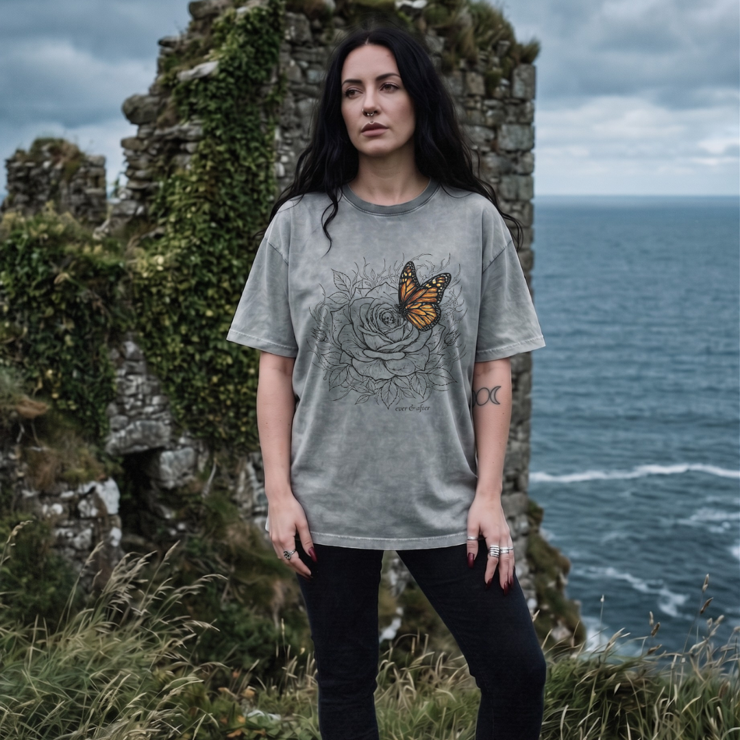 Woman wearing a gray t-shirt with a graphic design standing in front of ocean cliffs.