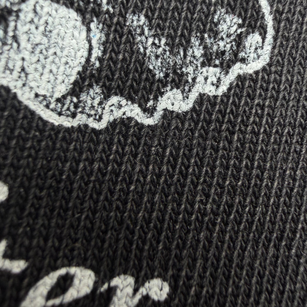 Close-up of a dark charcoal gray knit fabric with a distressed white graphic print showing part of a circular design and lettering.