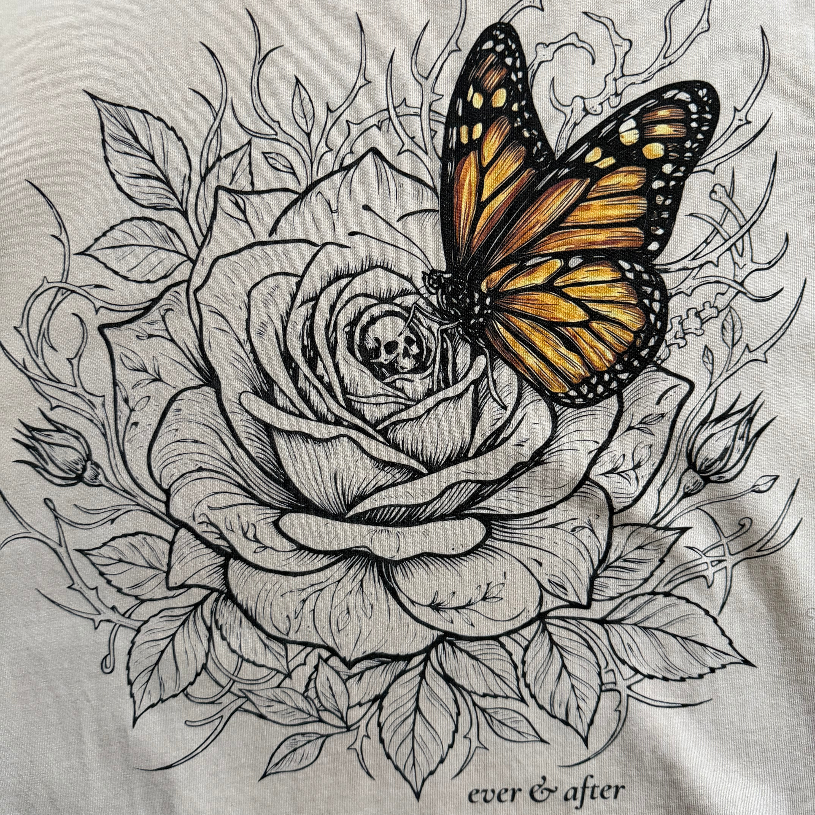 close up detail of rose and butterfly design on beige tee