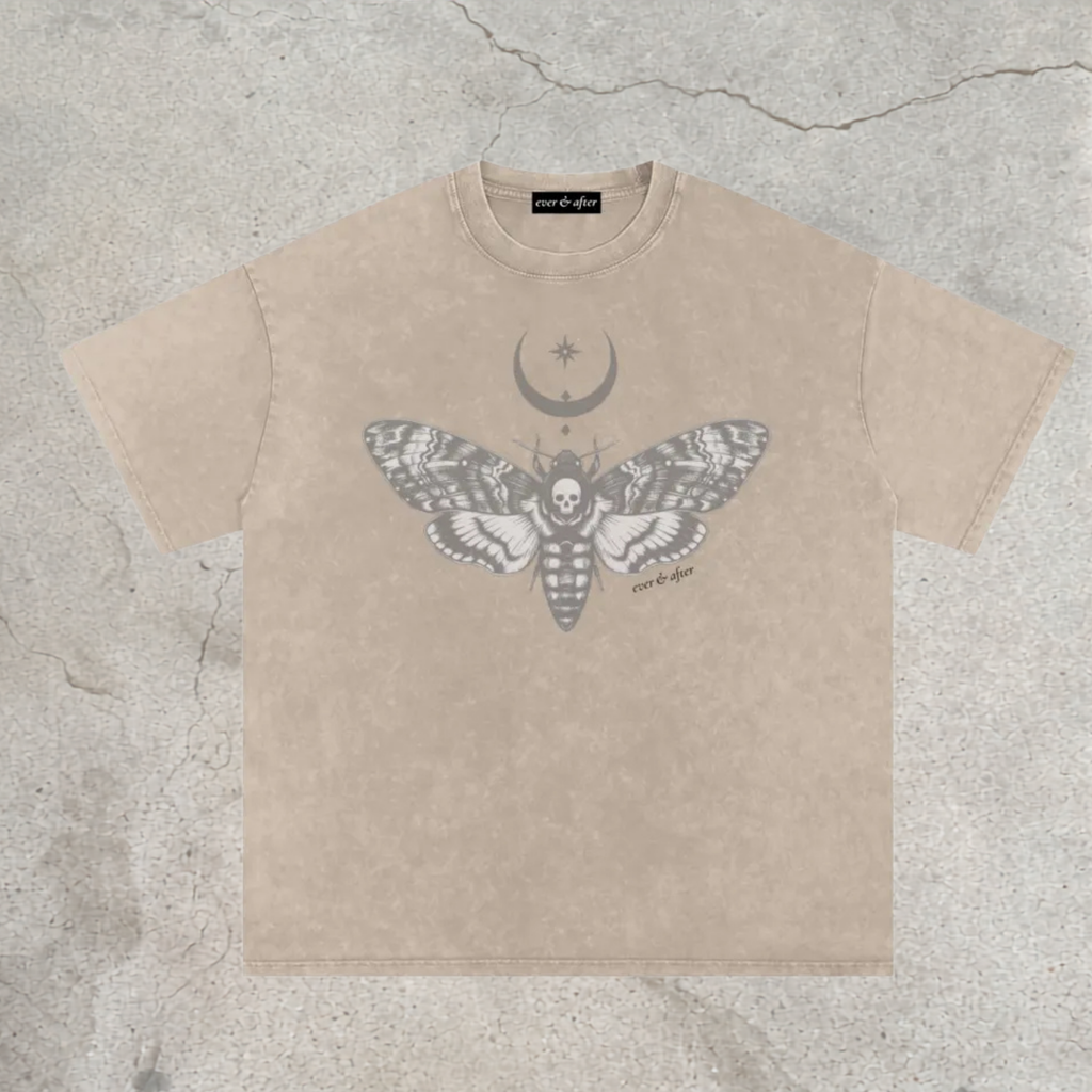 A beige short-sleeve t-shirt with a gray graphic of a moth, a crescent moon, and a star on the front, laid flat on a textured concrete background. The brand name 'monstera' is visible on the inner neck label.