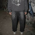 A person viewed from behind wearing a dark gray hoodie with a large white graphic print on the back, paired with dark sweatpants and white sneakers, standing in front of a graffiti-covered wall.