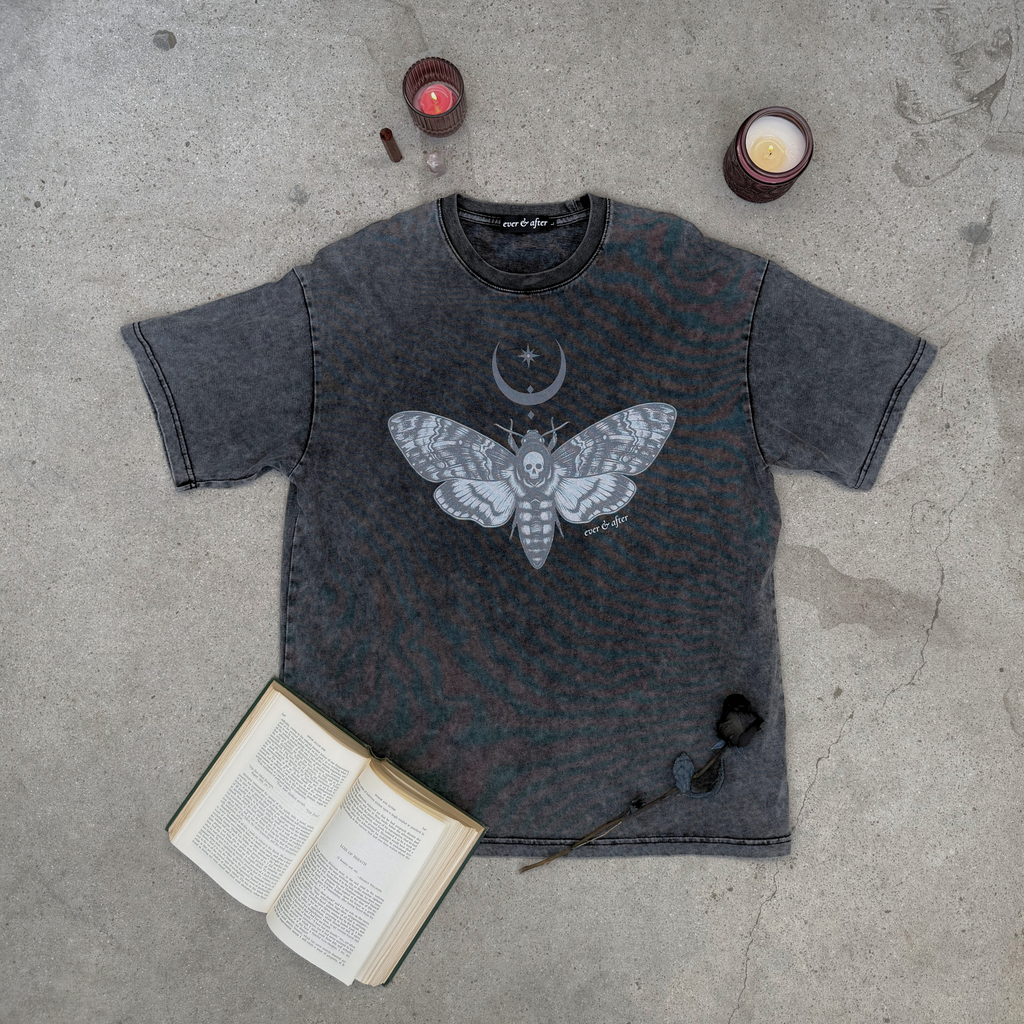 gothic stone oversized moth tee lay flat on concrete with rose, candles, old book, and crystals.