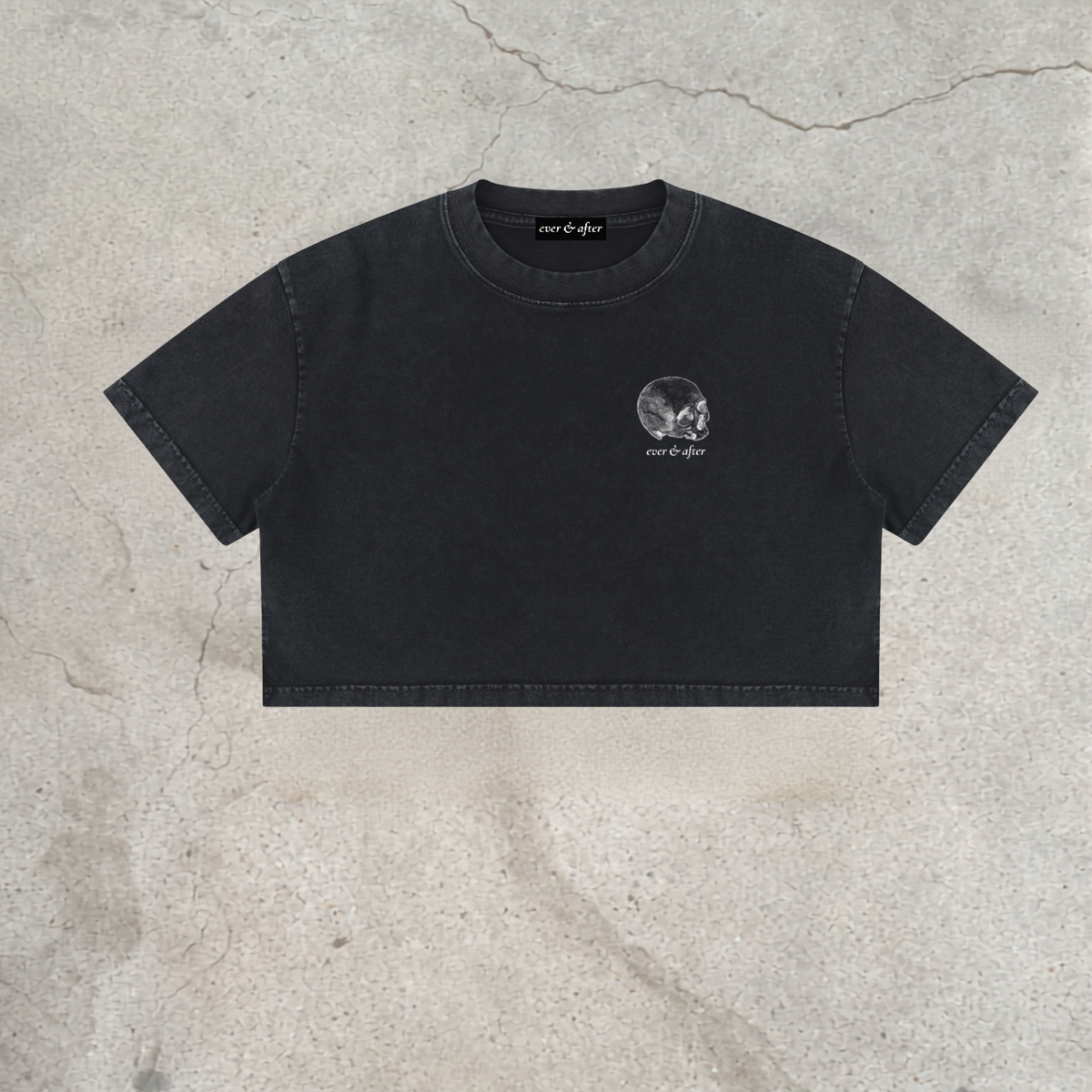A black cropped t-shirt with a small white skull graphic on the left chest, laid flat on a textured concrete background. The brand name 'pure of liar' is visible on the inner neck label and next to the graphic.