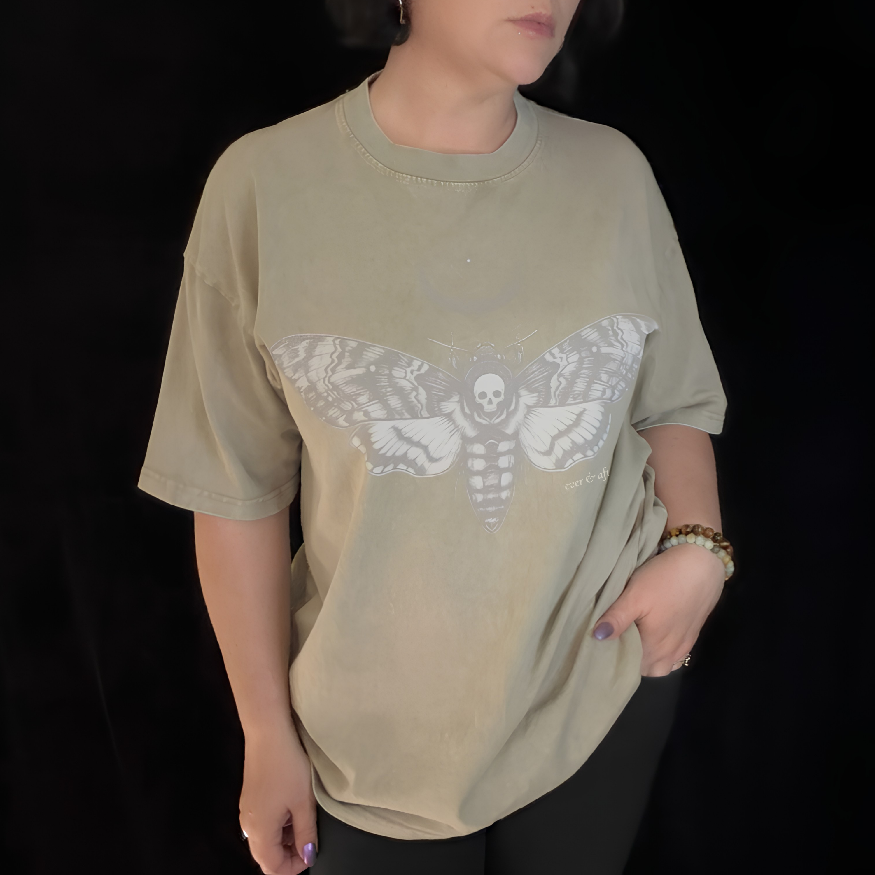 alt millennial woman wearing snow wash bone wash oversized tee with moth and moon design center on chest and brand word mark underneath