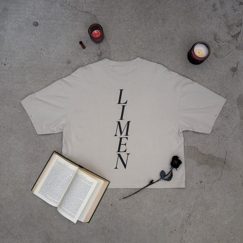 White t-shirt with 'LIMEN' text on a concrete surface with candles and an open book.