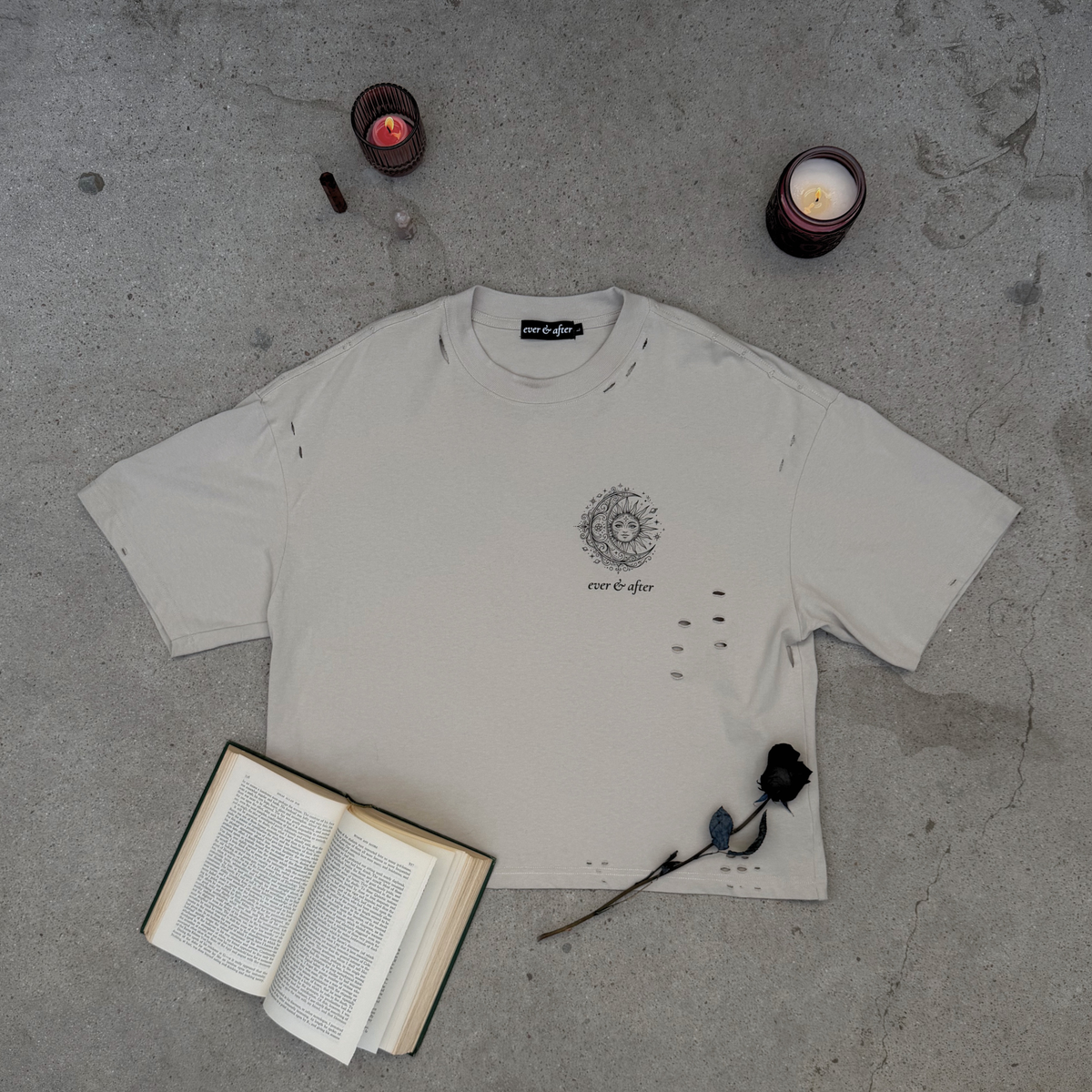 White t-shirt with a design on a gray surface with candles and an open book.