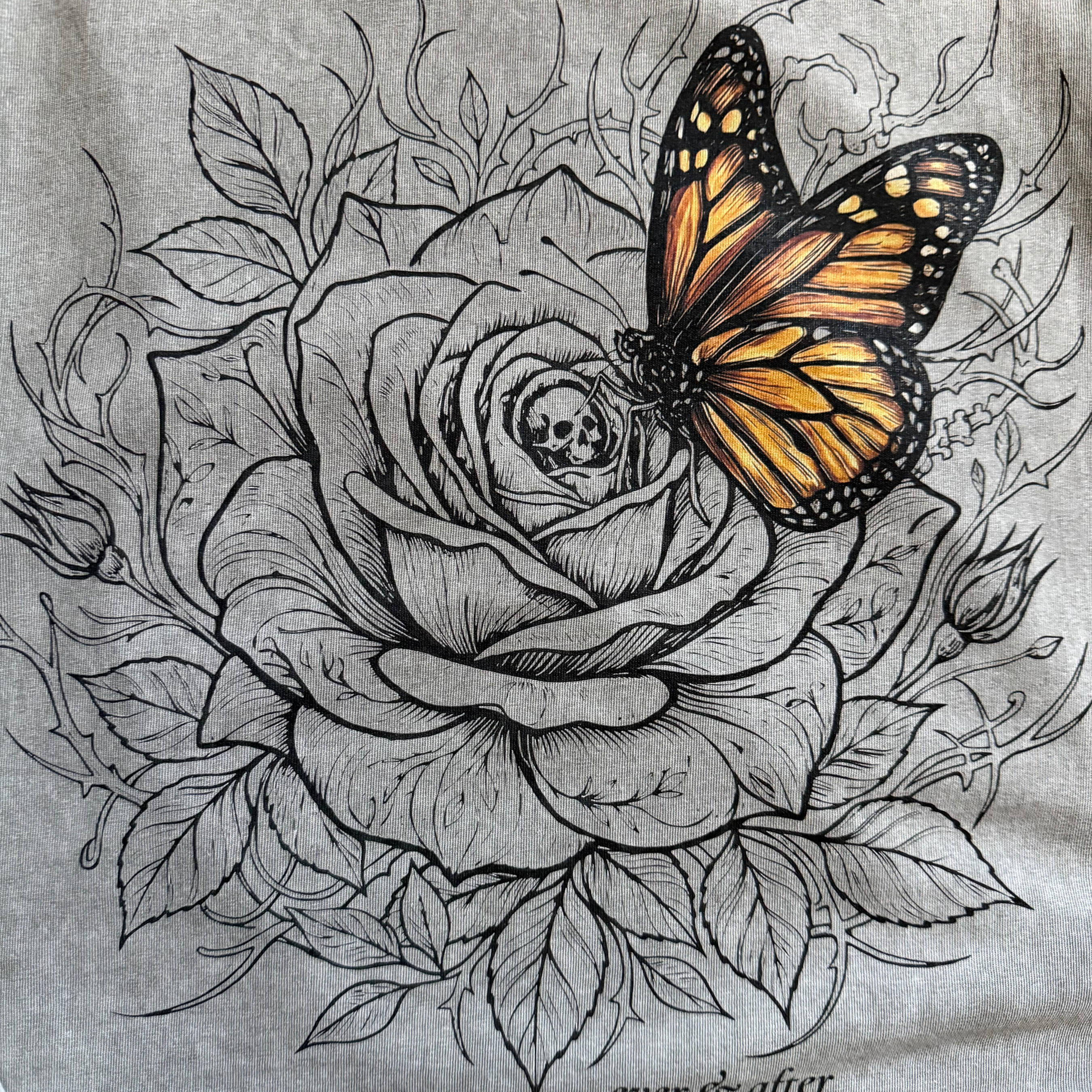 close up detail of rose and butterfly design on light gray tee