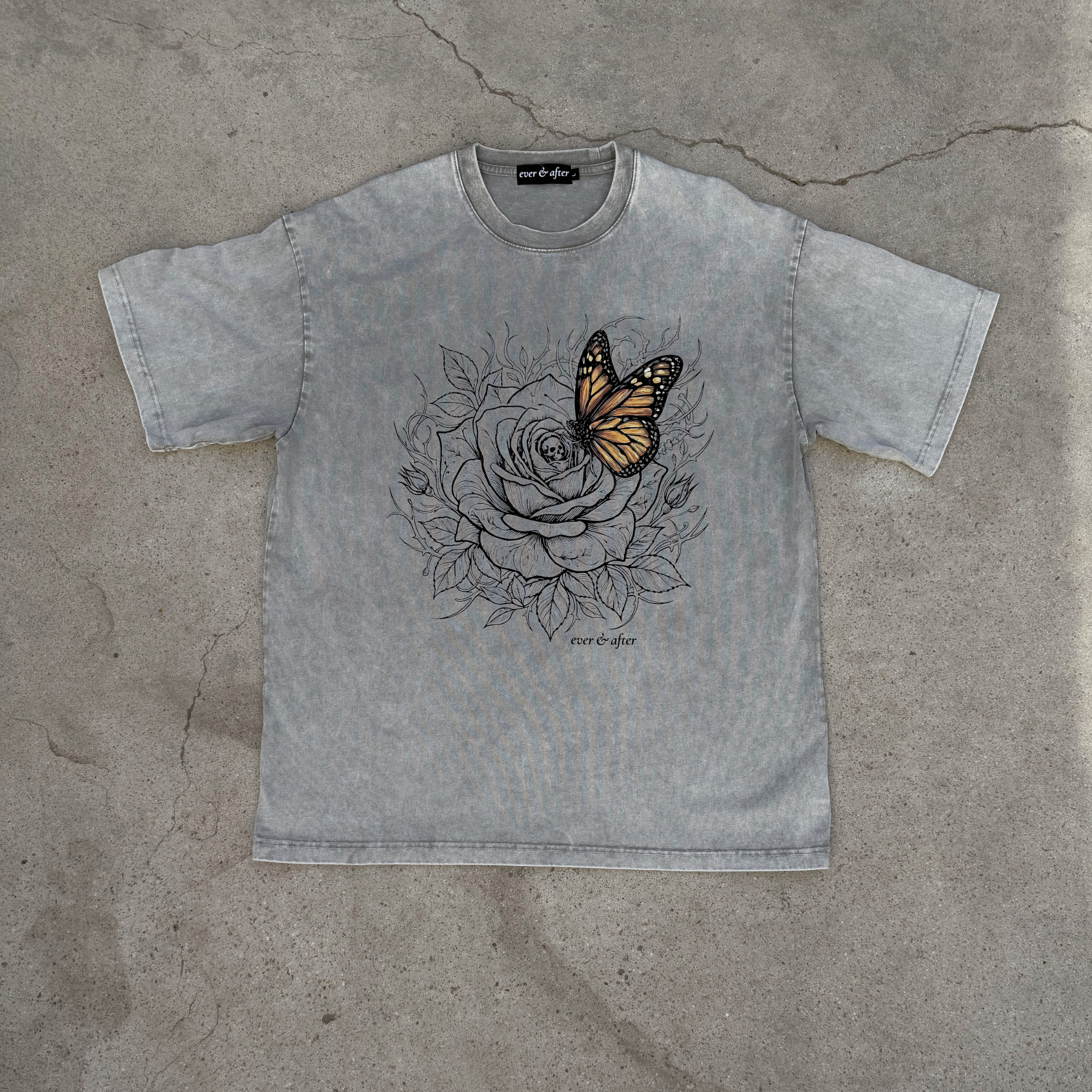 Gray t-shirt with a butterfly and rose design on a concrete surface