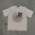 White t-shirt with a butterfly and rose design on a gray concrete surface
