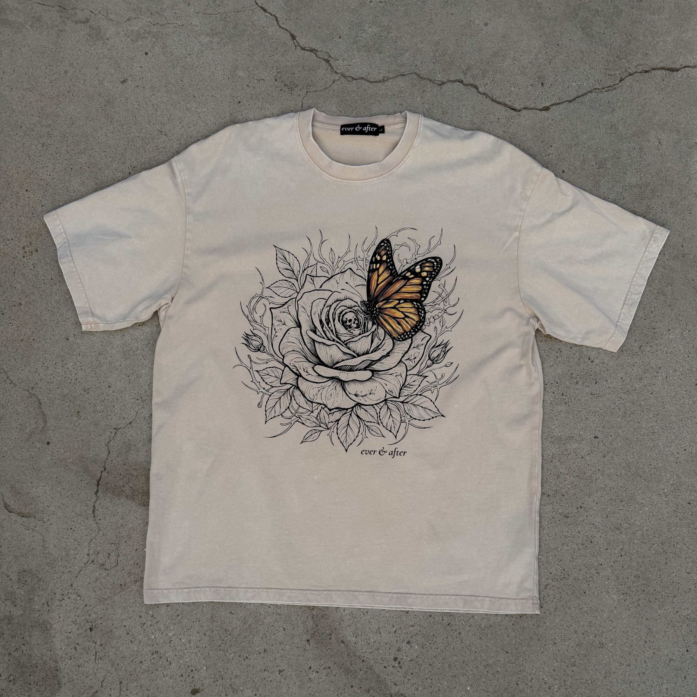 White t-shirt with a butterfly and rose design on a gray concrete surface