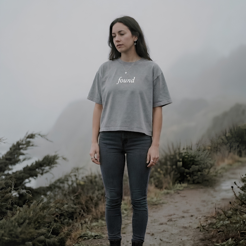alt millennial woman standing on a foggy path wearing light gray boxy tee with text found on the center chest