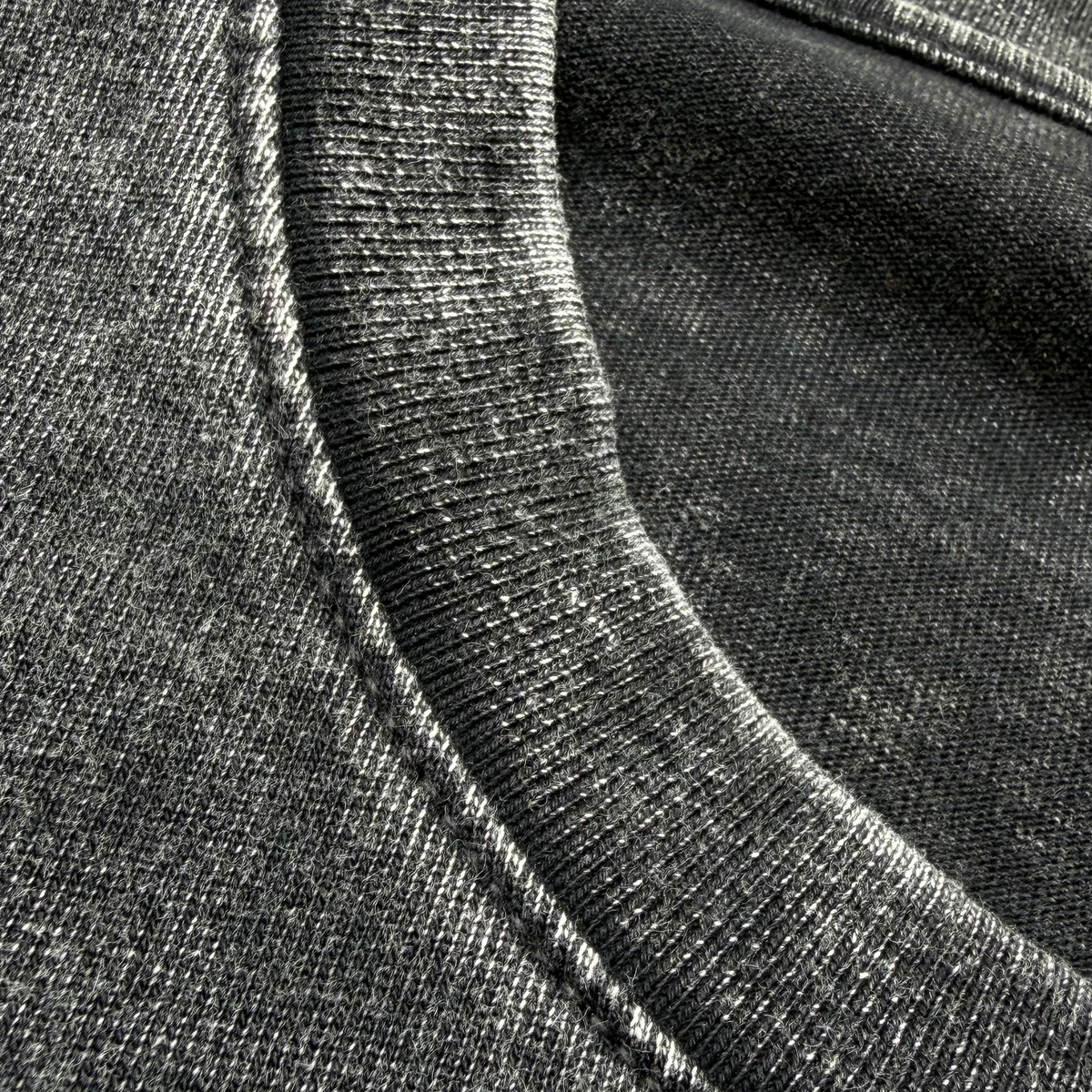 Close-up of a dark gray heathered cotton t-shirt fabric, showing the ribbed crew neck collar and textured weave.