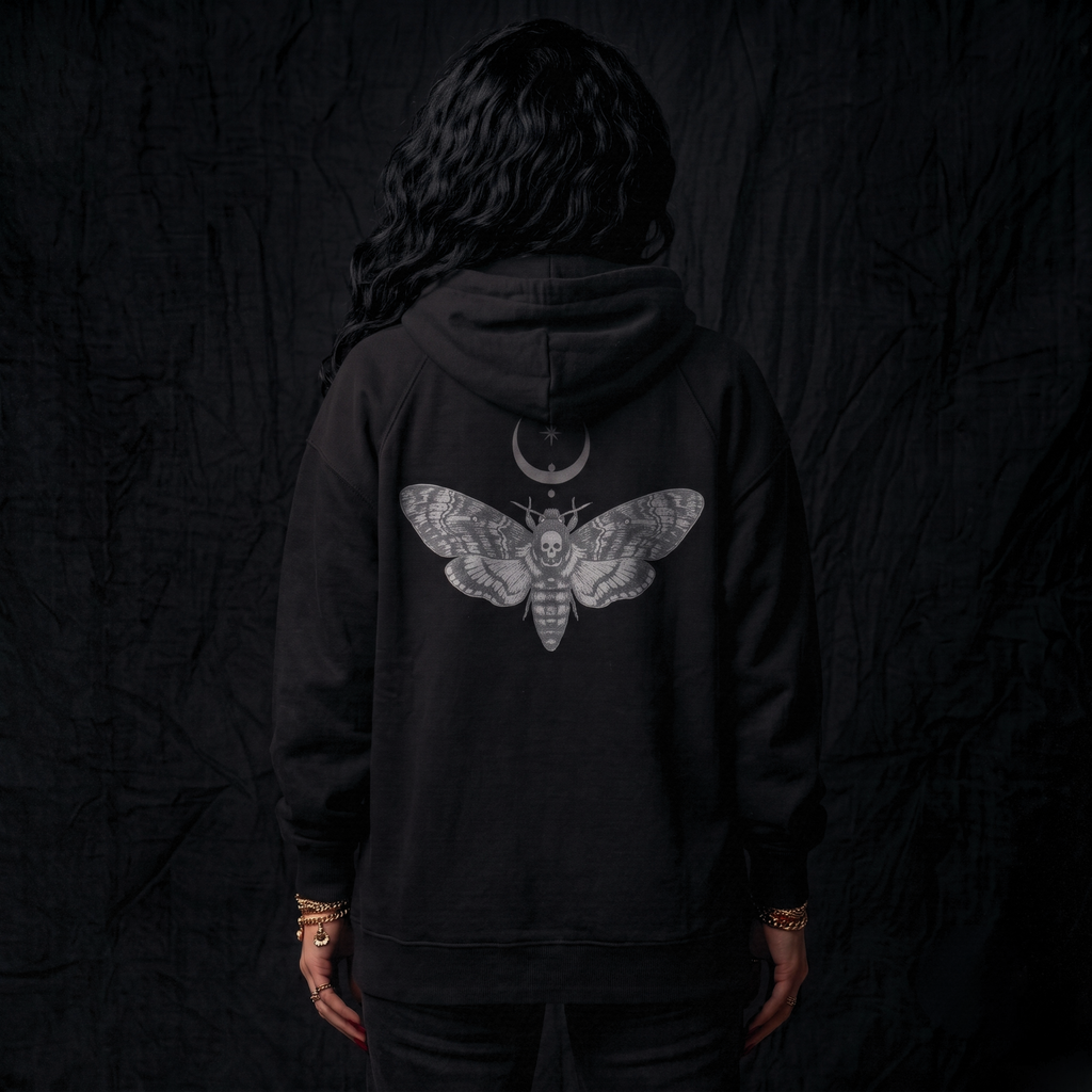 Person wearing a black hoodie with a moth design on the back against a dark background