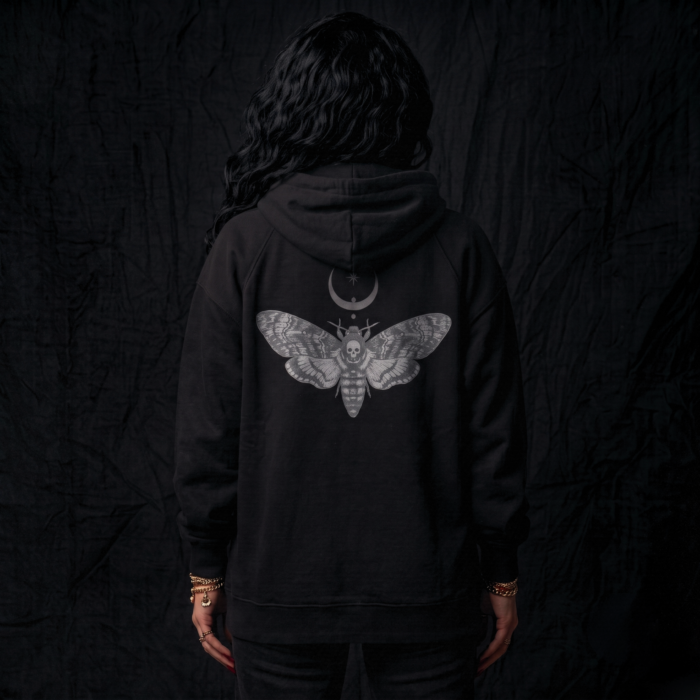 Person wearing a black hoodie with a moth design on the back against a dark background