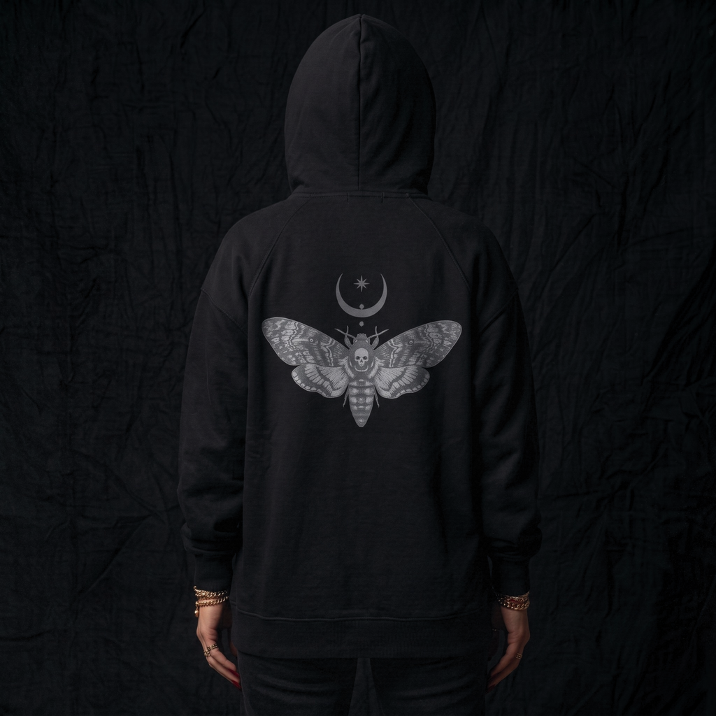 Black hoodie with a moth and moon design on the back against a dark background