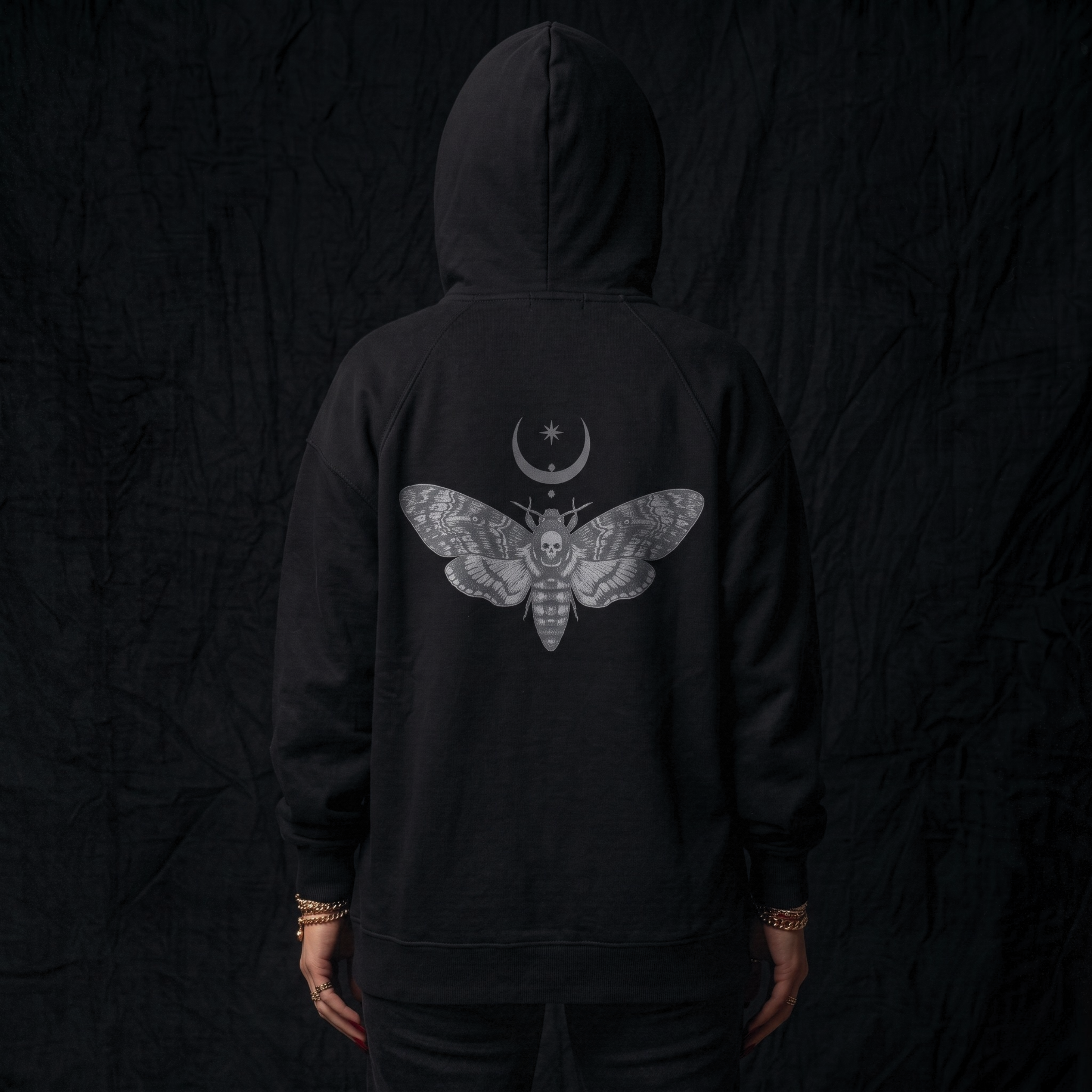 Black hoodie with a moth and moon design on the back against a dark background