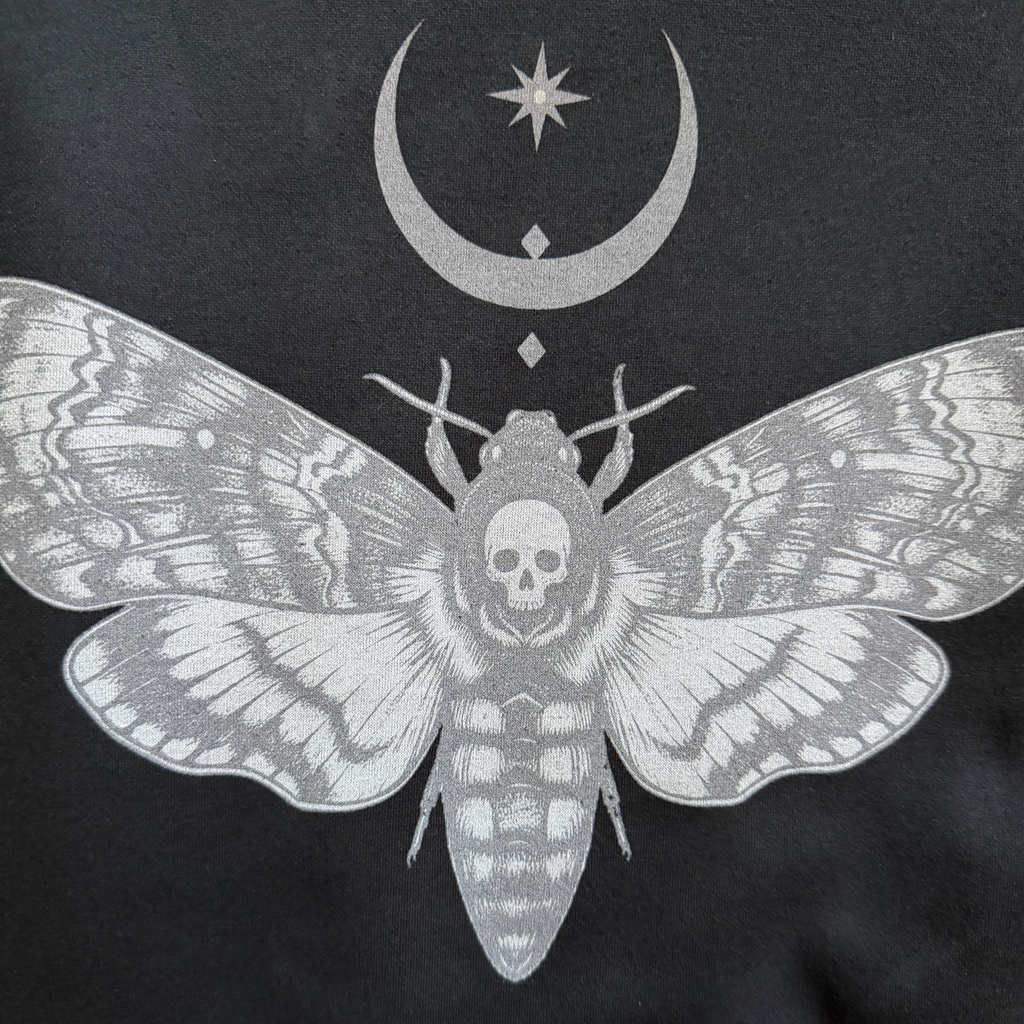 Black t-shirt with a white moth design featuring a skull and celestial symbols on a black background.