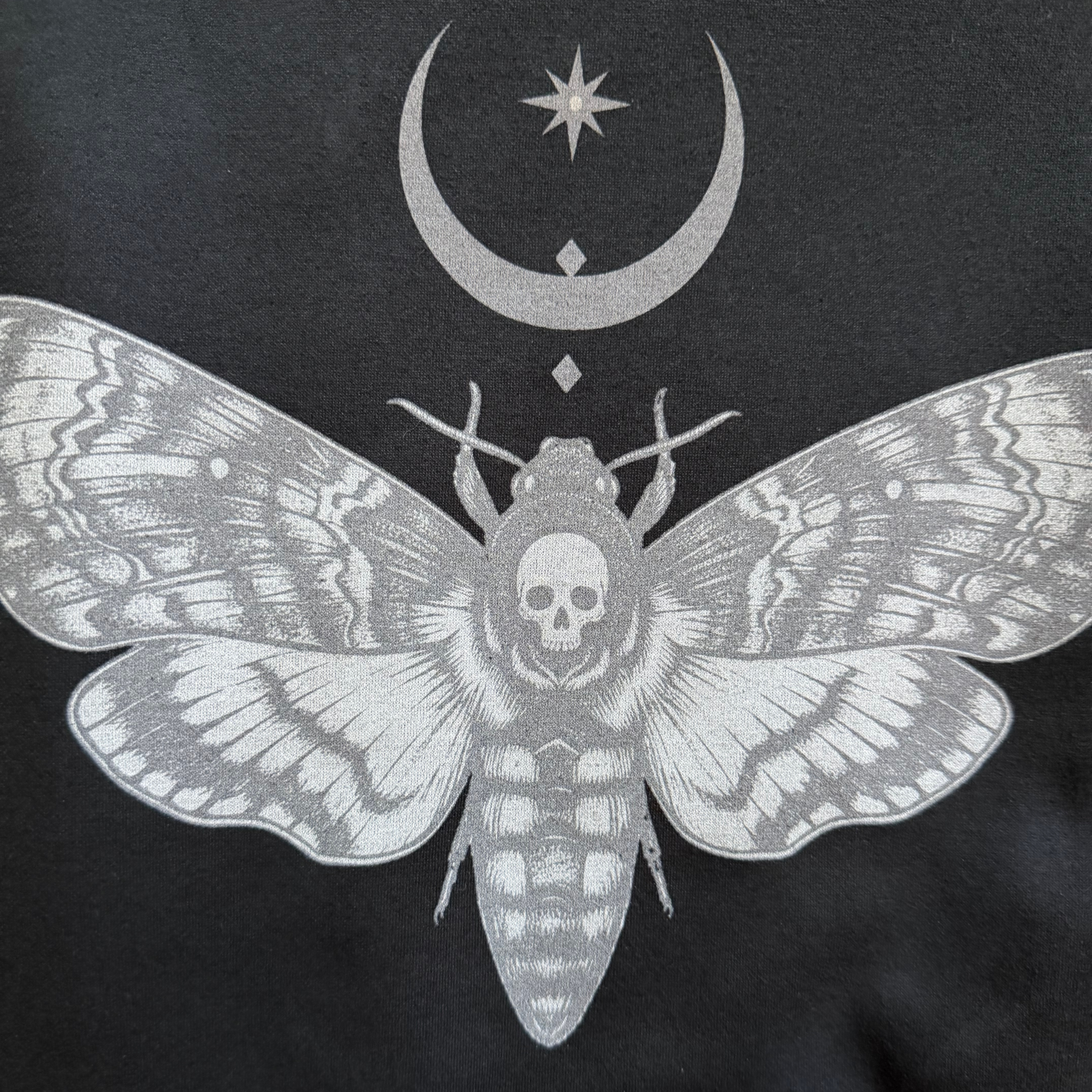 Black t-shirt with a white moth design featuring a skull and celestial symbols on a black background.
