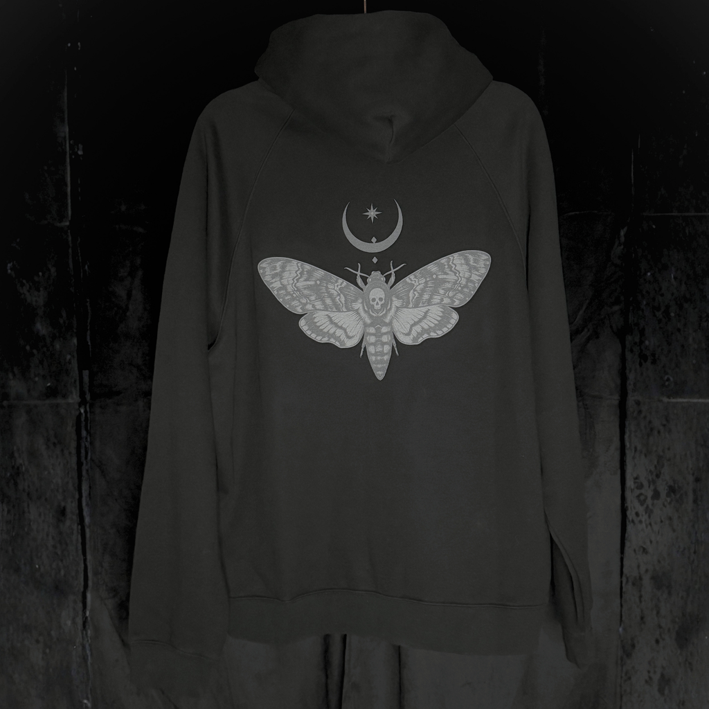 Black hoodie with a moth and moon design on the back against a dark background