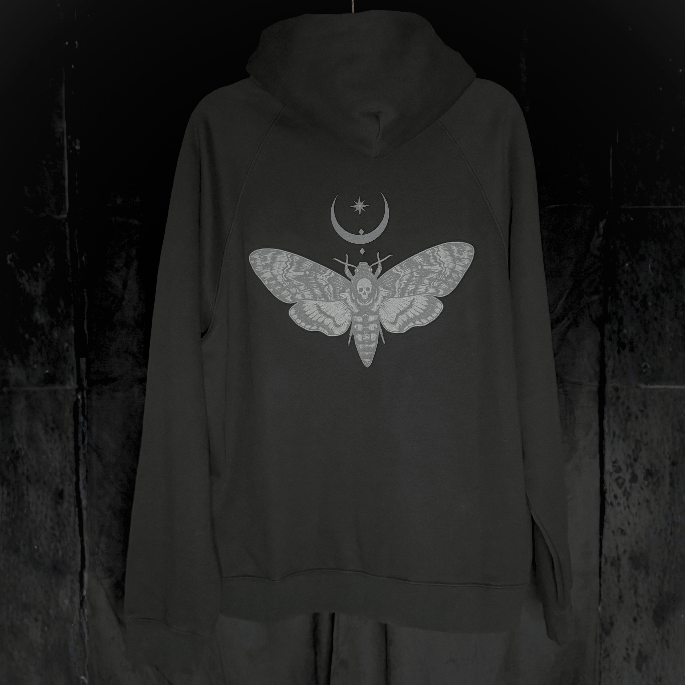 Black hoodie with a moth and moon design on the back against a dark background